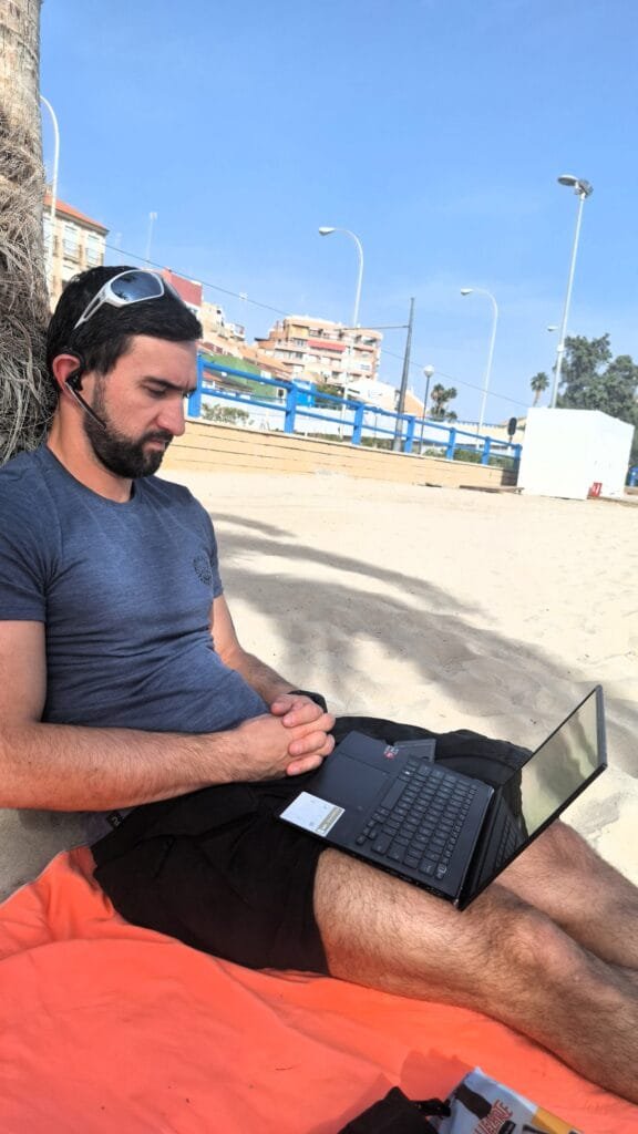 Adam from Millennials Do Travel working on a travel itinerary on a beach in Alicante, Spain.