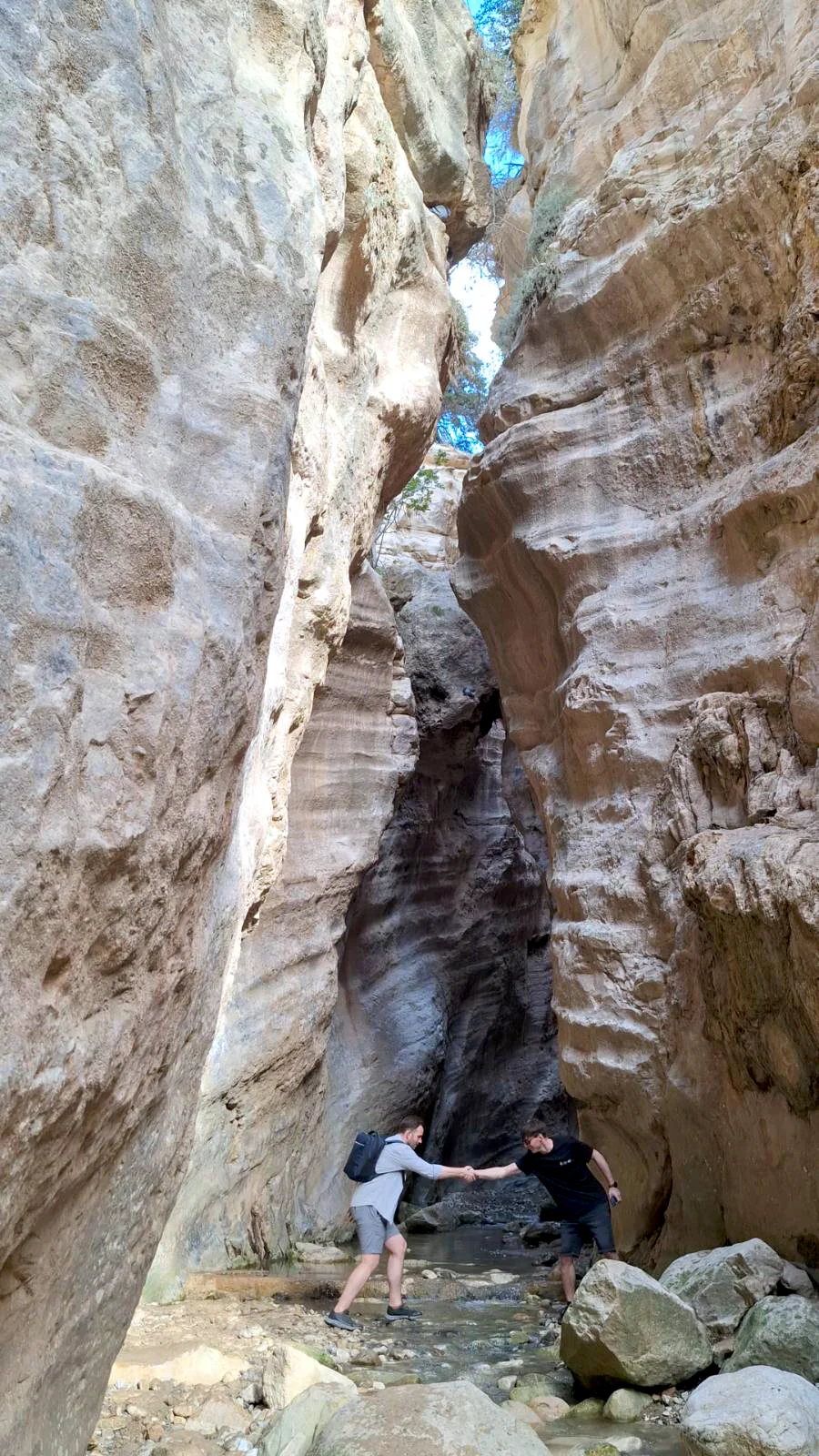 Two hikers helping each other to pass the river inside the narrow limestone walls of Avakas Gorge, Cyprus.