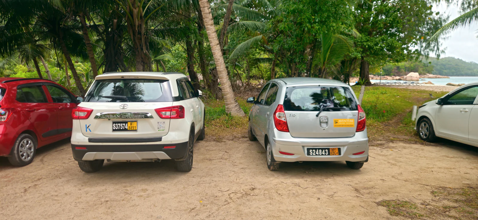 Comparison of a large Toyota SUV and a small rental car parked under palm trees in Seychelles.