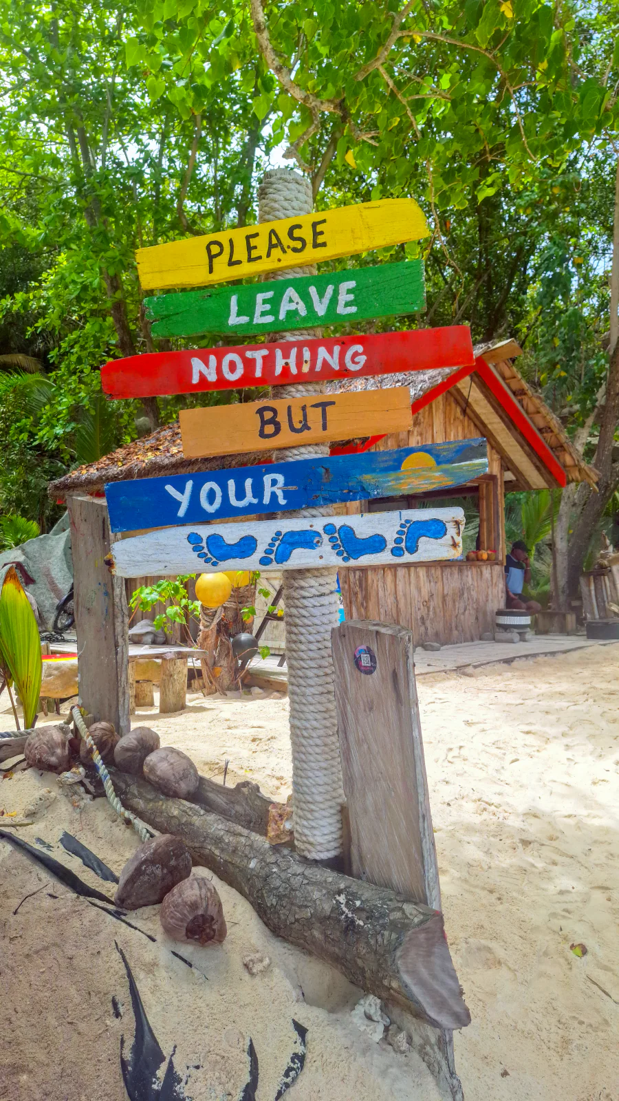 Colorful wooden sign saying 'Please leave nothing but your footprints' on a La Digue beach.