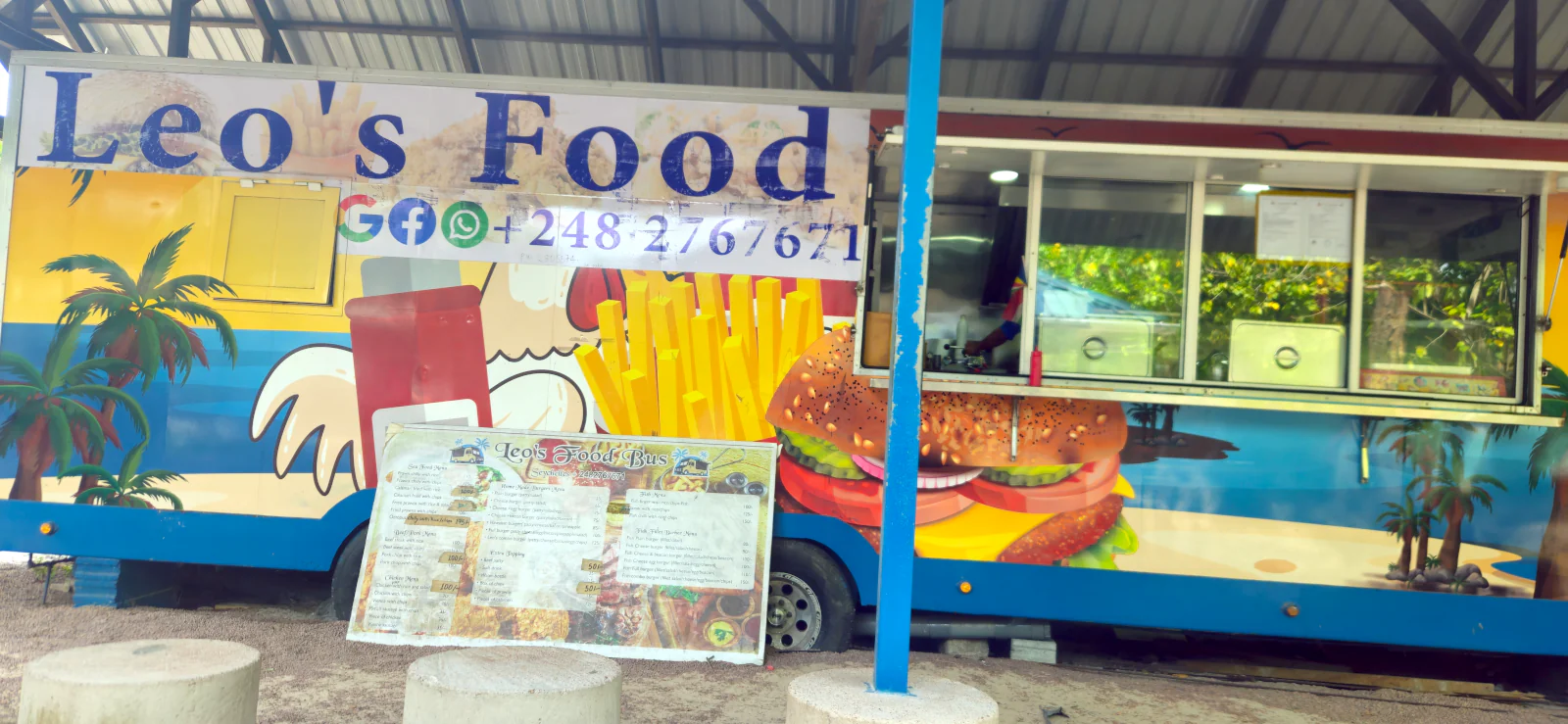 Kolorowy food truck Leo's Food Bus zaparkowany przy plaży Cote D'Or na Praslin, serwujący kreolskie jedzenie.