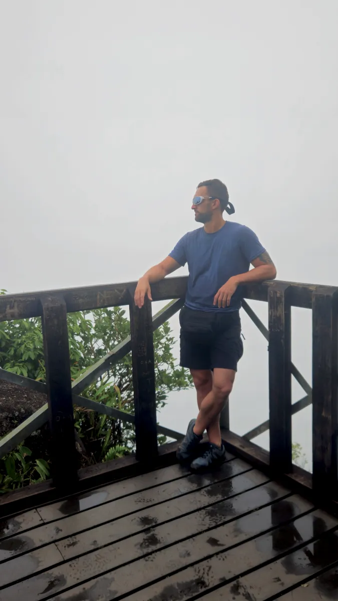 Adam from Millennials Do Travel standing on the wooden viewpoint deck of Morne Blanc trail shrouded in thick mountain fog on Mahé.