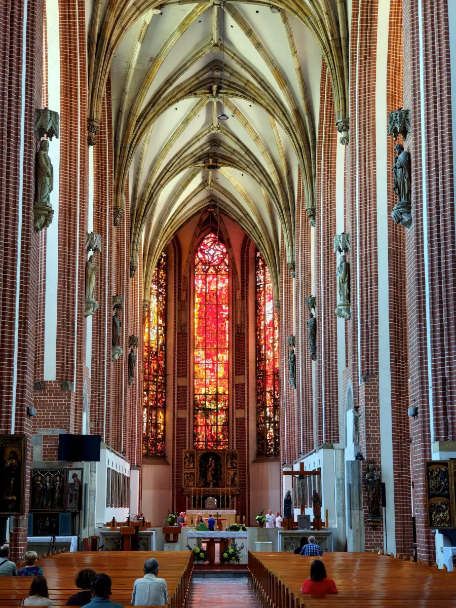 Interior of the Gothic Church of Our Lady on Piasek Island in Wrocław with high brick vaults and red stained glass altar.
