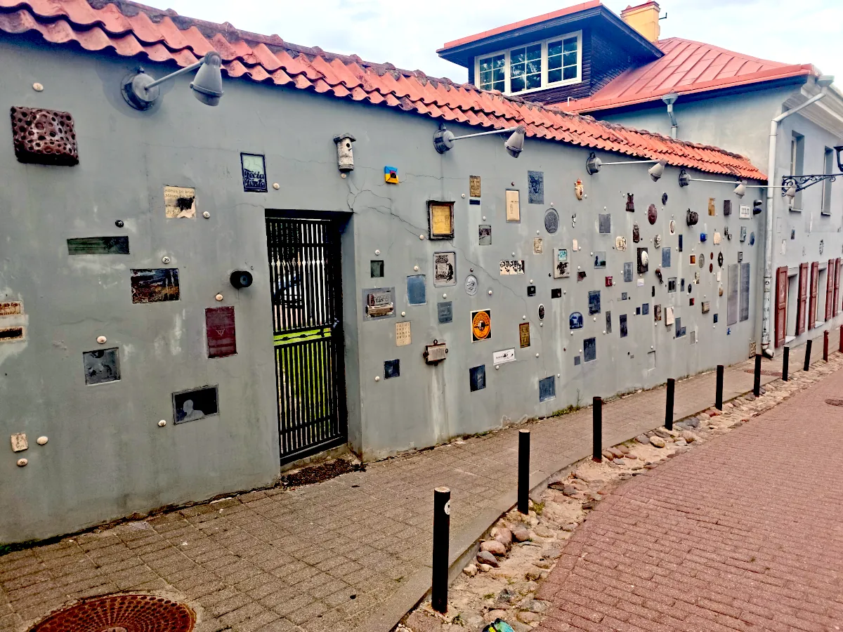 A grey street wall embedded with small artworks and plaques dedicated to literary figures on Literatų street in Vilnius.