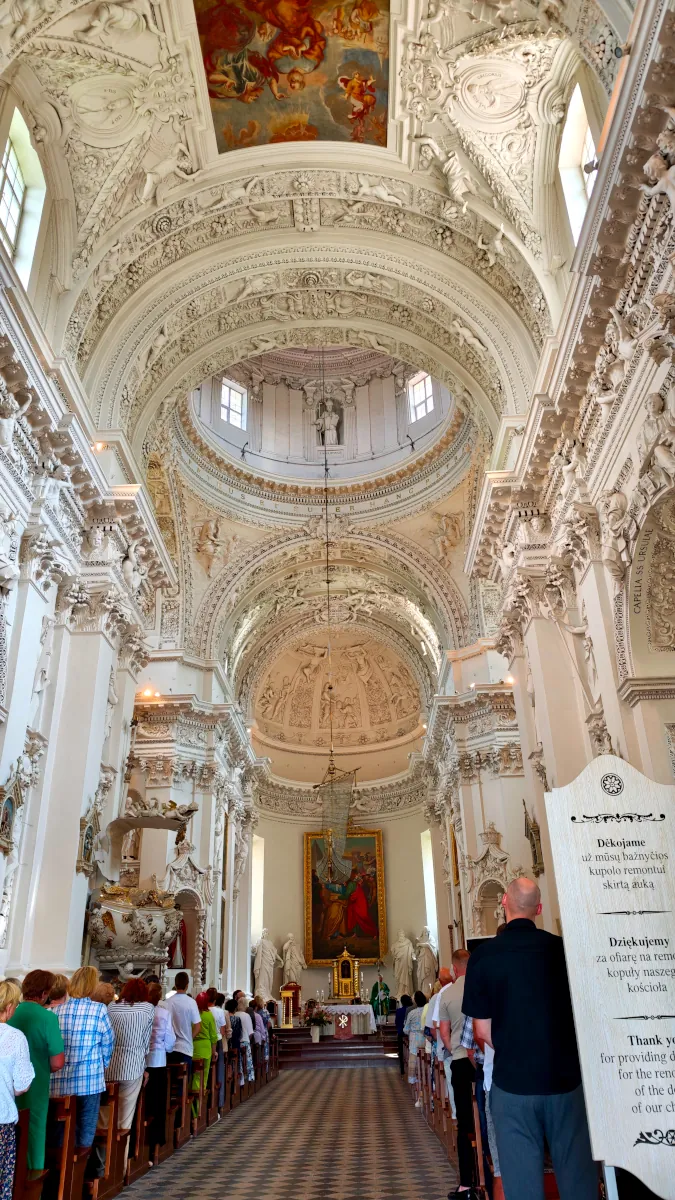 Intricate white stucco carvings and dome interior of St. Peter and Paul's Church in Antakalnis, Vilnius during Mass.