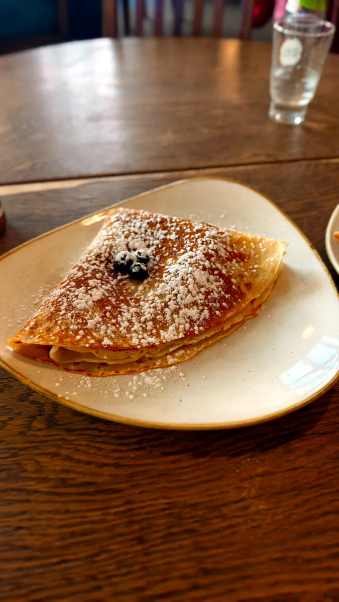 A large golden folded pancake dusted with powdered sugar and topped with blueberries served on a plate at Pub Kompressor in Tallinn Old Town.